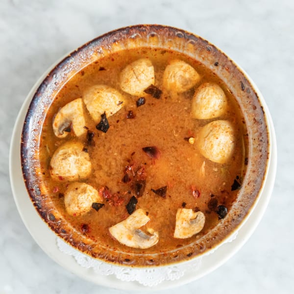Overhead view of a bowl of Phattra Thai Tom Yum soup with mushrooms and spices.