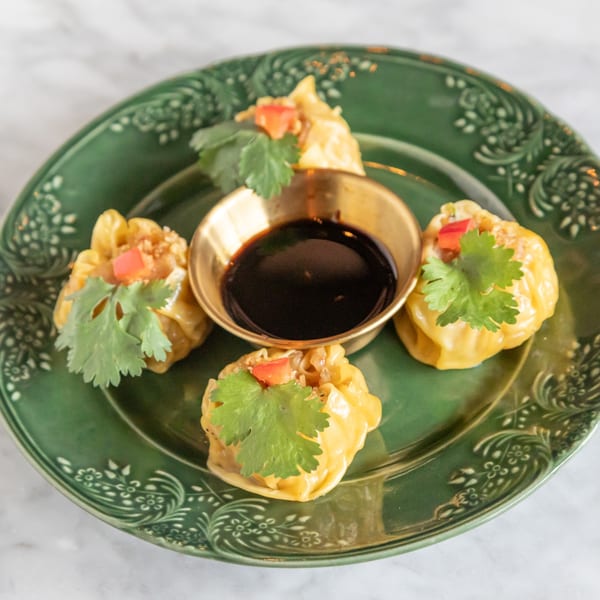 Four Phattra Thai dumplings with cilantro and red pepper on a green plate with dipping sauce.