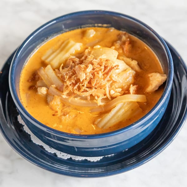 A blue bowl of Phattra Thai red curry with chicken, bamboo shoots, and fried shallots.